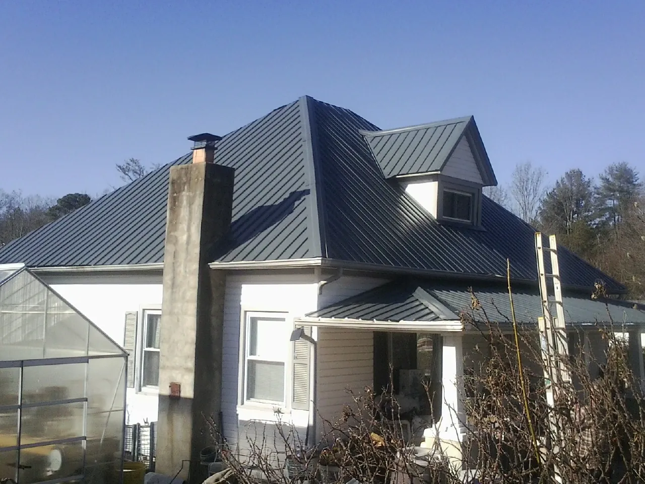 Dark blue standing seam metal roof on a white farmhouse with dormer — Slate & Tile Roof Repair by Roofing Brothers in Wentzville