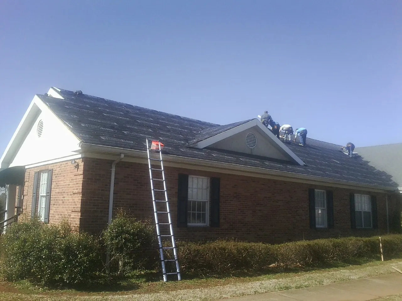 Crew tearing shingles off a brick ranch roof with a ladder set — Emergency Roof Repair work by our crew in Wentzville