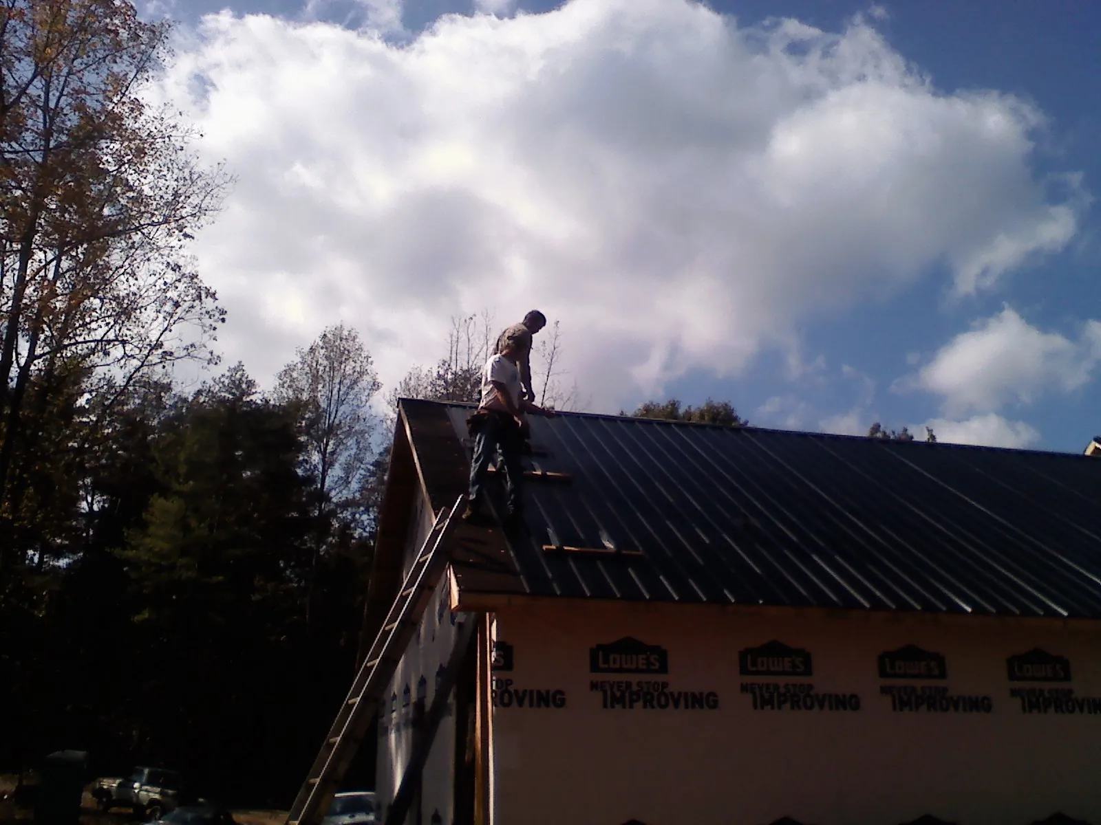 Roofer fastening dark metal panels high against a cloudy sky, from a Roof Inspection job in Wentzville