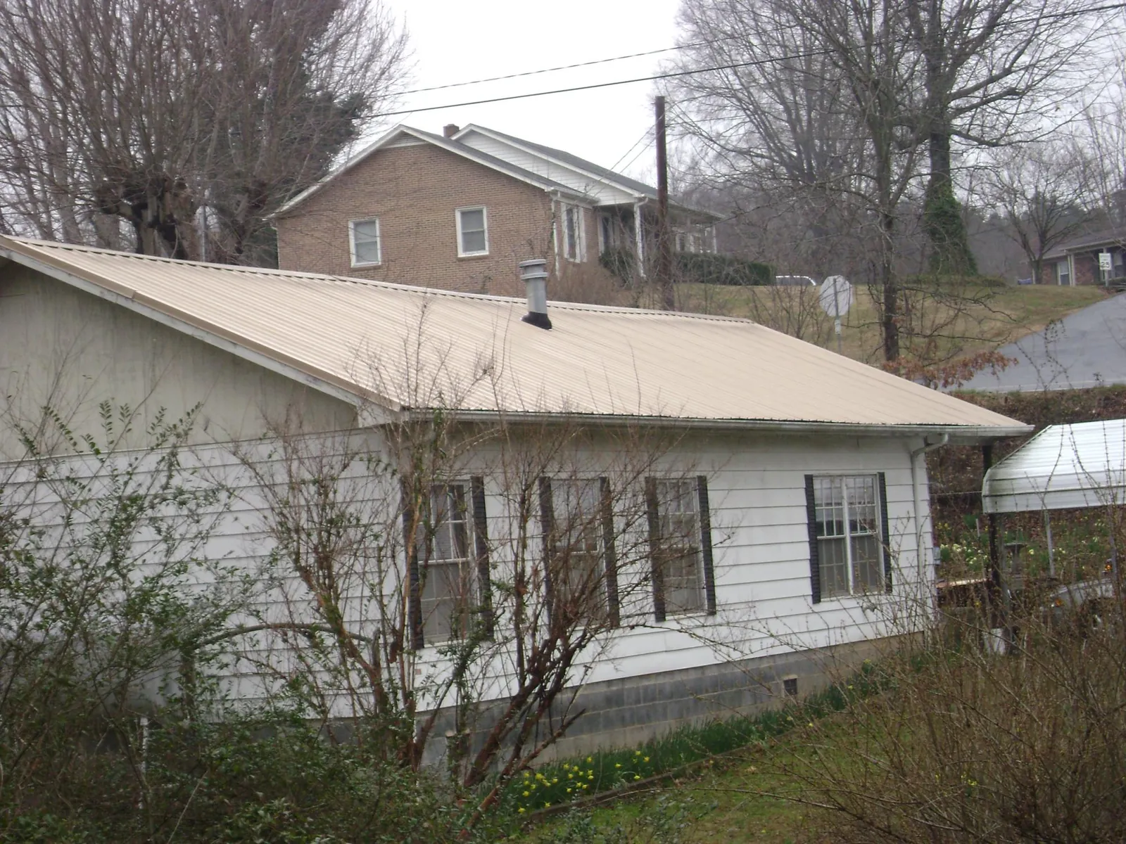 Tan metal roof on a white sided house set into a hillside — Commercial Roofing by Roofing Brothers in Wentzville